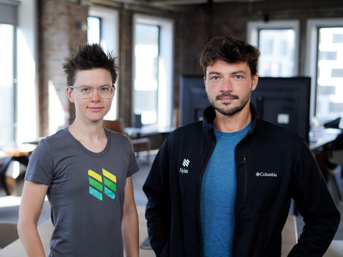 Christine Spang, cofounder and CTO of Nylas (left), and Gleb Polyakov, cofounder and CEO of Nylas (right). Spand is wearing a branded tshirt, and Gleb is wearing a blue tshirt with a black jacket on top. They are standing in an office space.