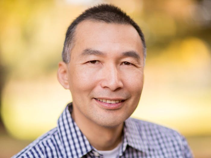 Headshot of Eric Ly, founder of KarmaCheck, with a checkered button up shirt and a yellow blurred background