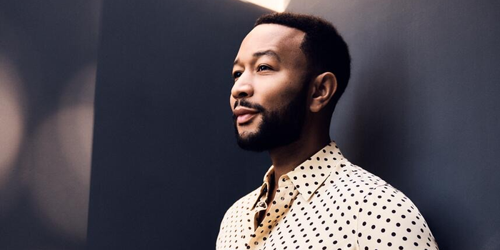 Headshot of John Legend, wearing a black and white shirt with red pants