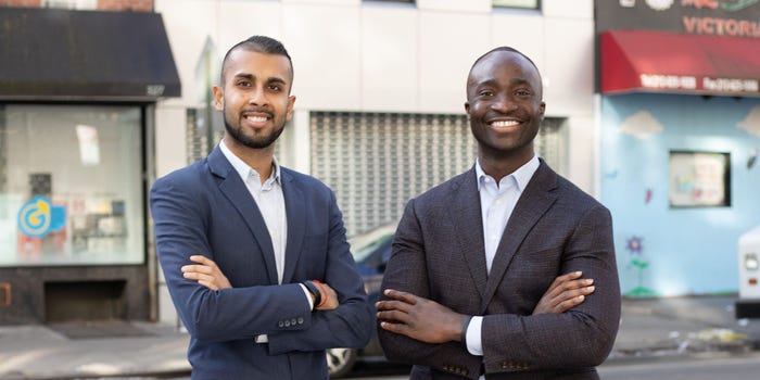 Samir Goel and Abbey Wemimo, cofounders of Esusu, standing outside wearing suits, with stores in the background.